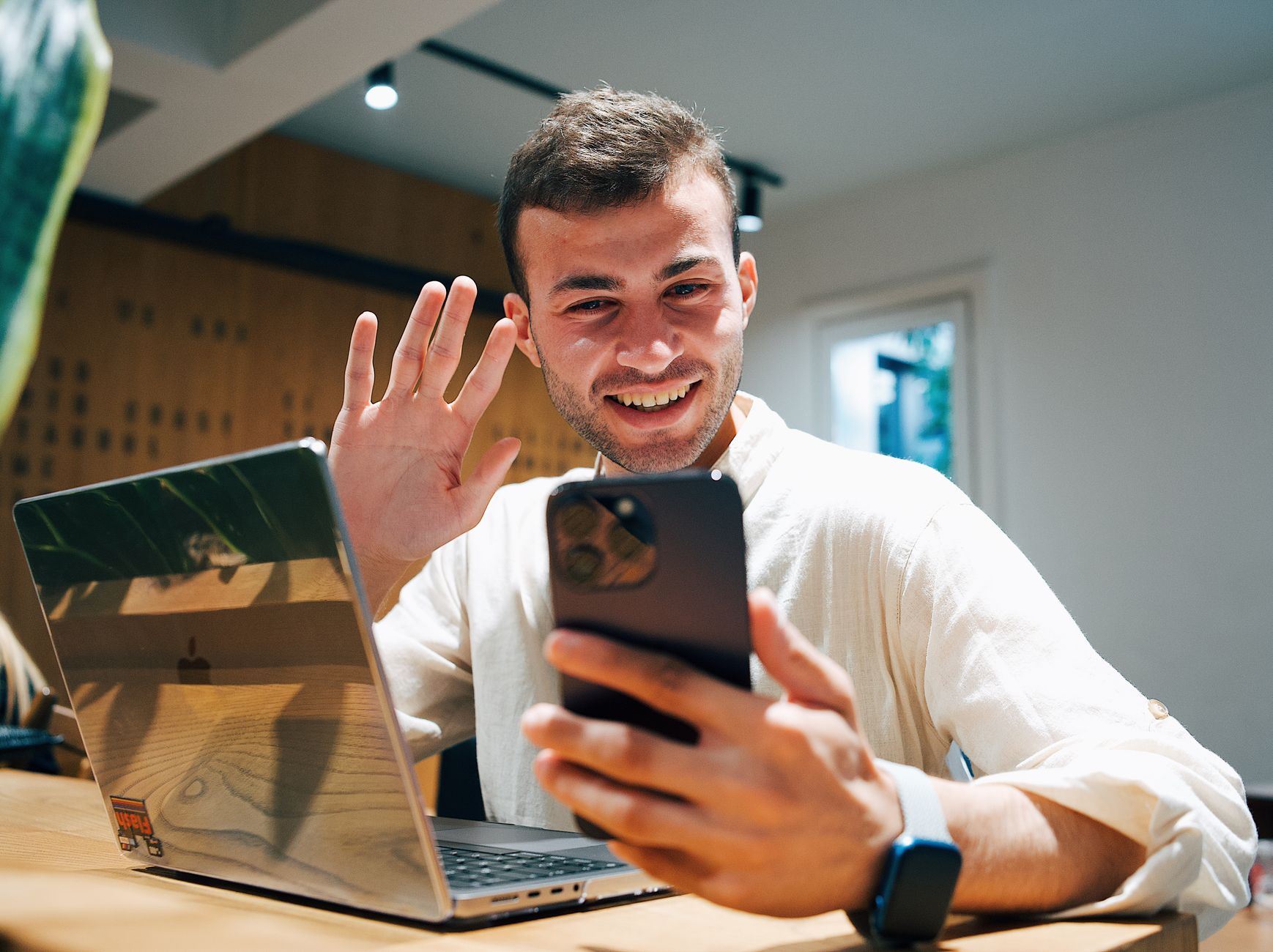 A person in a cafe comparing videos on a phone and a laptop.